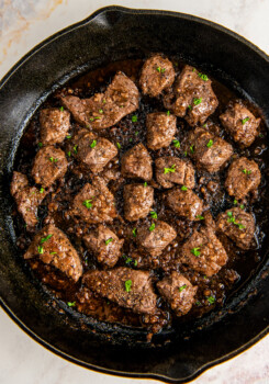 Overhead view of steak bites cooking in a sauce in a skillet.