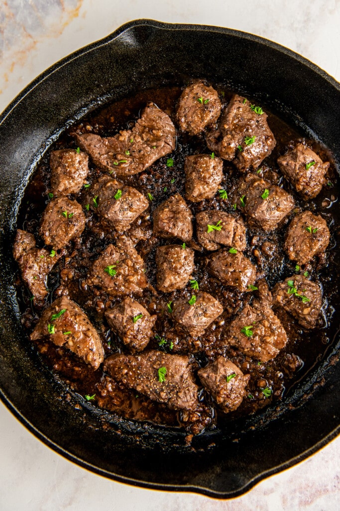 Overhead view of steak bites cooking in a sauce in a skillet.