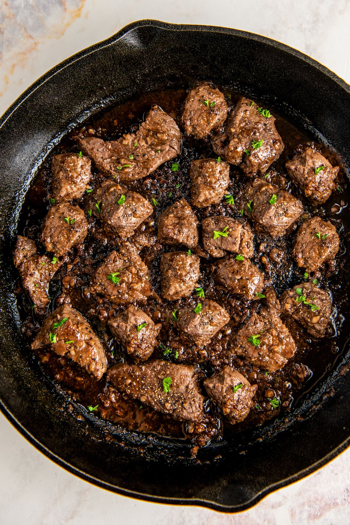 Overhead view of garlic butter steak bites cooking in a sauce in a heavy bottomed skillet.