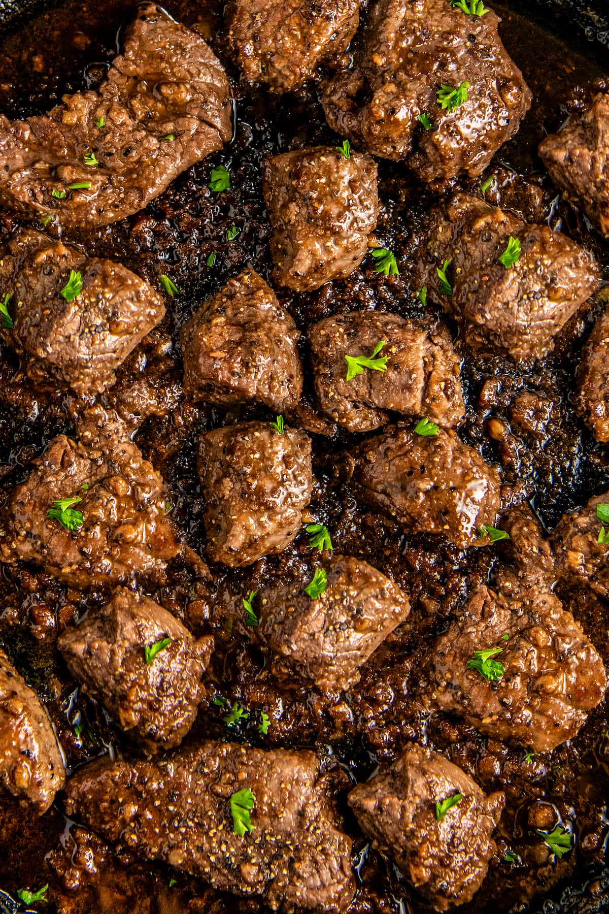 Close up overhead view of steak bites with garlic butter cooking in a cast iron skillet.