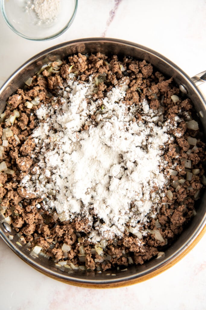 Overhead view of a pot of cooked ground beef and onions topped with flour.