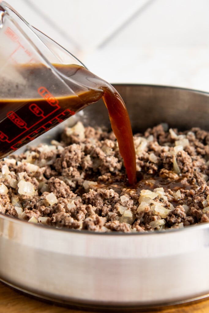 Beef broth being poured into a pot of ground beef.