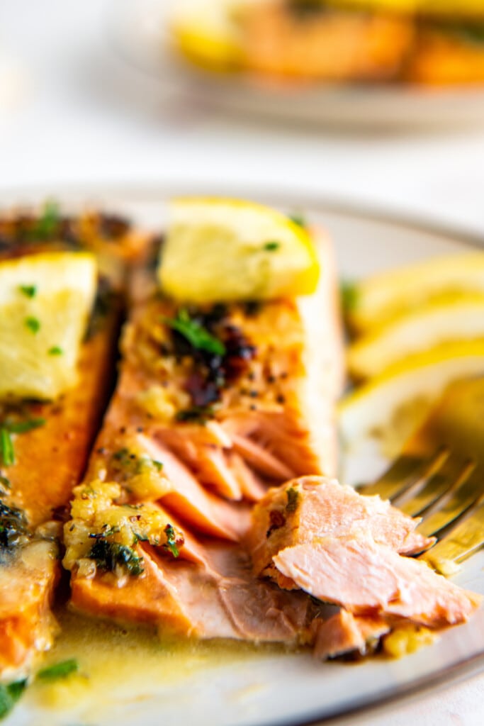 A plate with two fillets of salmon topped with lemon and parsley, with a fork removing a piece from one.