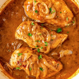 Overhead view of a pot filled with three chicken breasts, gravy, and onions.