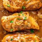 Overhead view of three chicken breasts smothered in onions and gravy, topped with parsley.