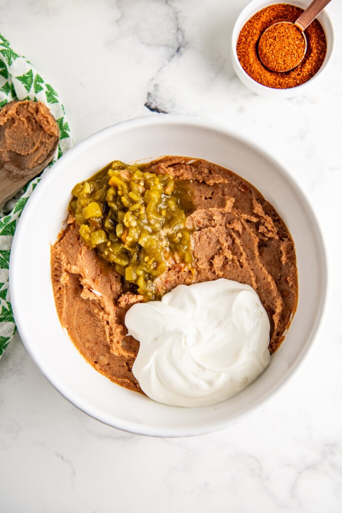 Mixing refried beans, sour cream, and green chilis together in a bowl