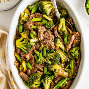 A white serving dish filled with beef and broccoli garnished with green onions and sesame seeds.