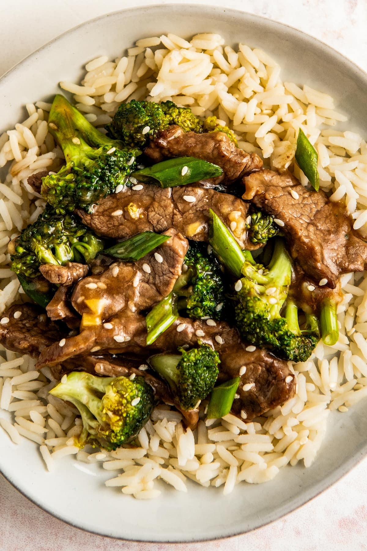 A white plate filled with rice and topped with broccoli and beef. 