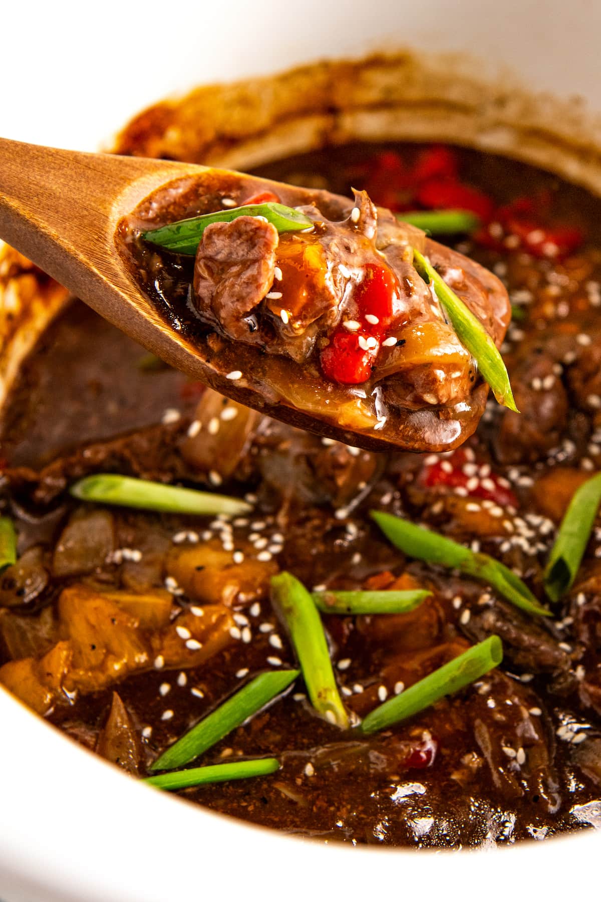 A wooden spoon dishing out a serving of crockpot pepper steak with bell peppers and onions smothered in a savory brown sauce.