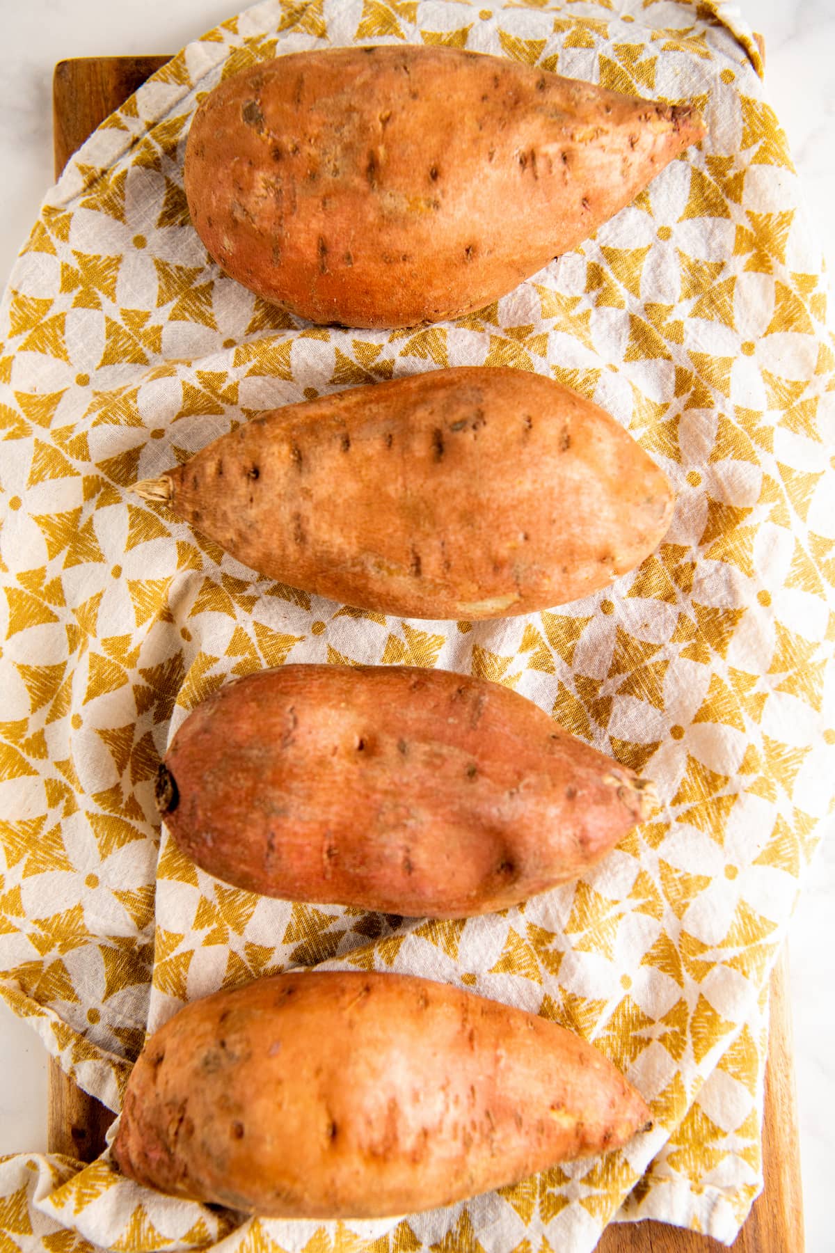 4 sweet potatoes set out on a yellow and white cloth.