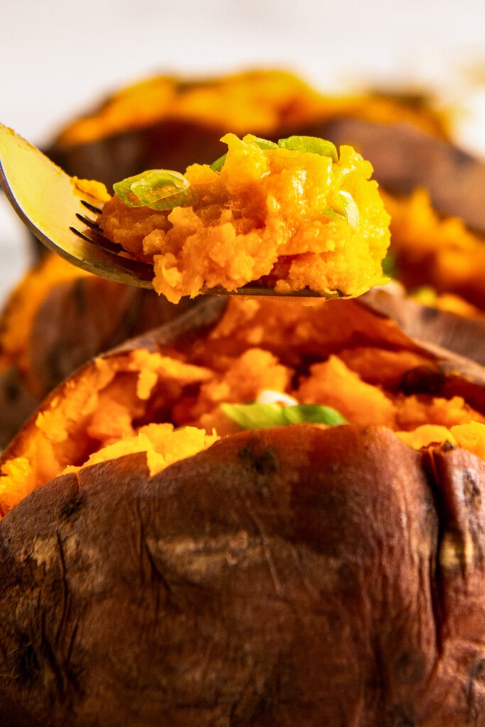 Someone taking a bite of crockpot sweet potatoes with a fork.