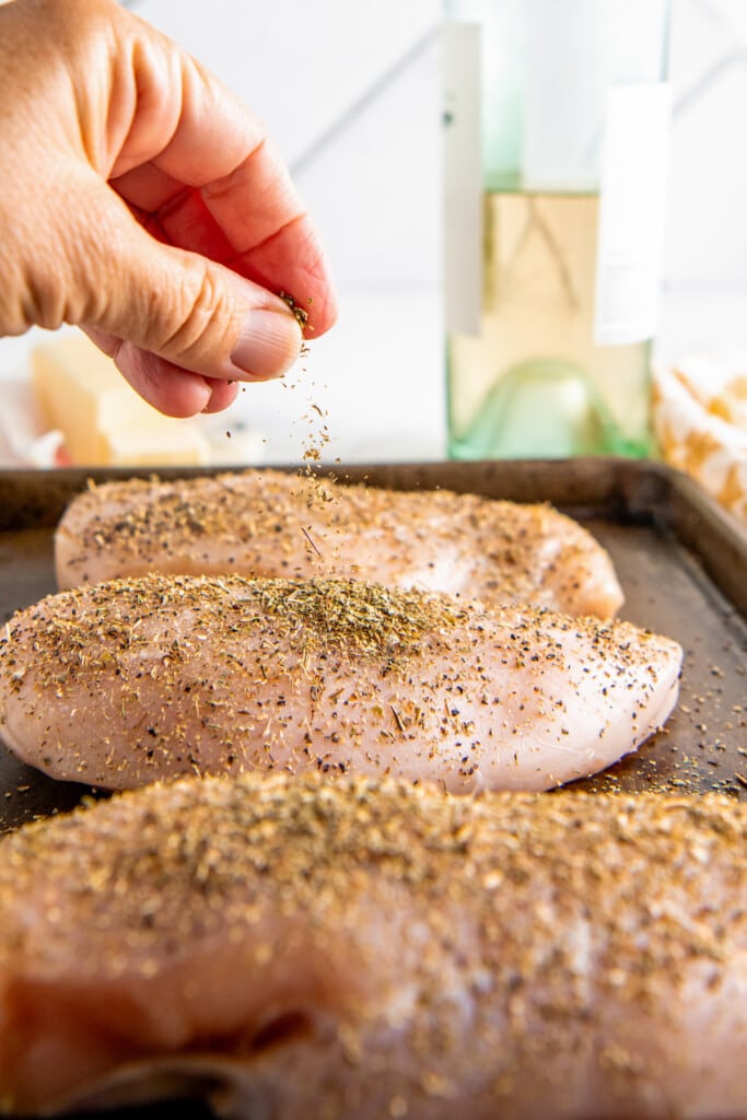 Seasoning chicken breast with salt, pepper, and Italian seasoning.