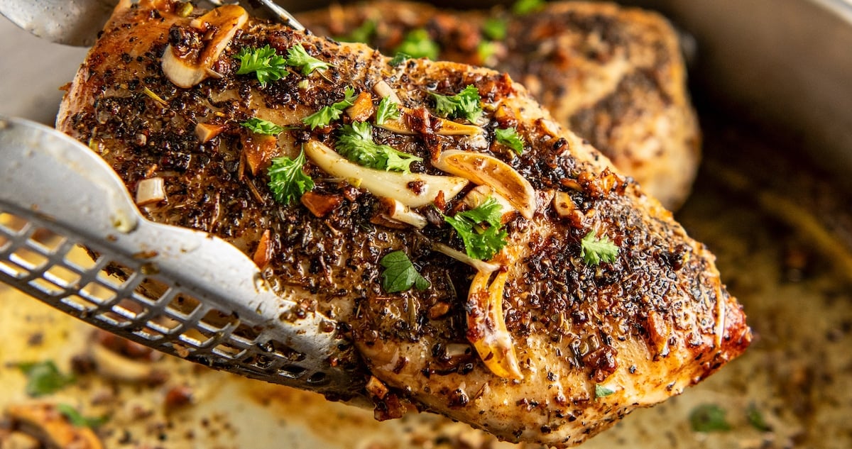 Using tongs to pull out a piece of garlic butter chicken.