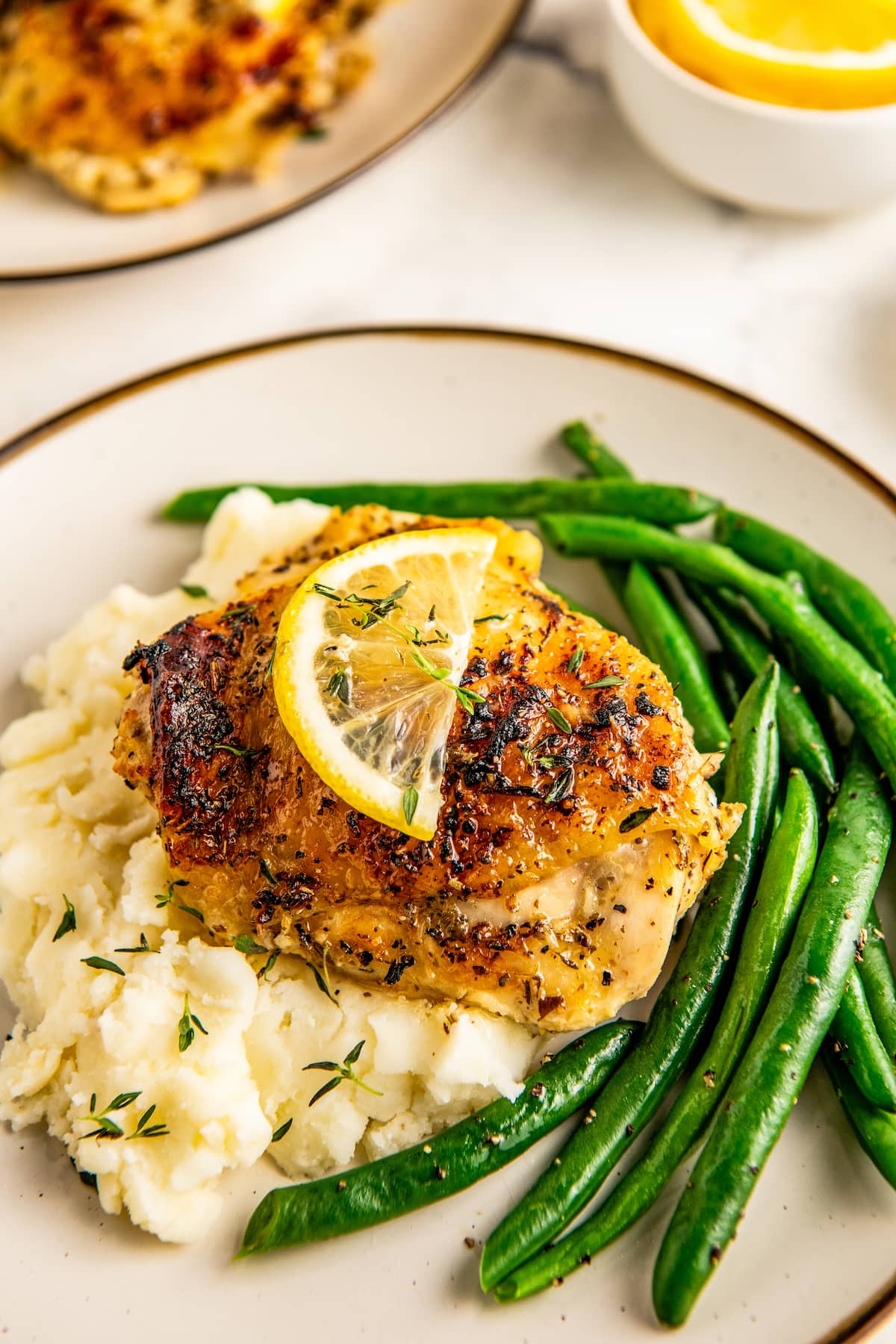 A top view of a plate with baked lemon pepper chicken with crispy skin over a side of mashed potatoes, and green beans.