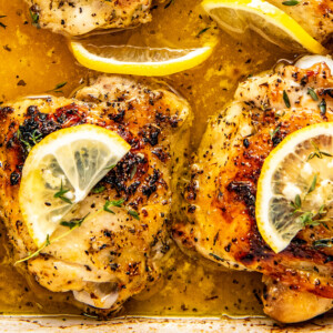 Roasted lemon pepper chicken in a pan with fresh lemon slices on top