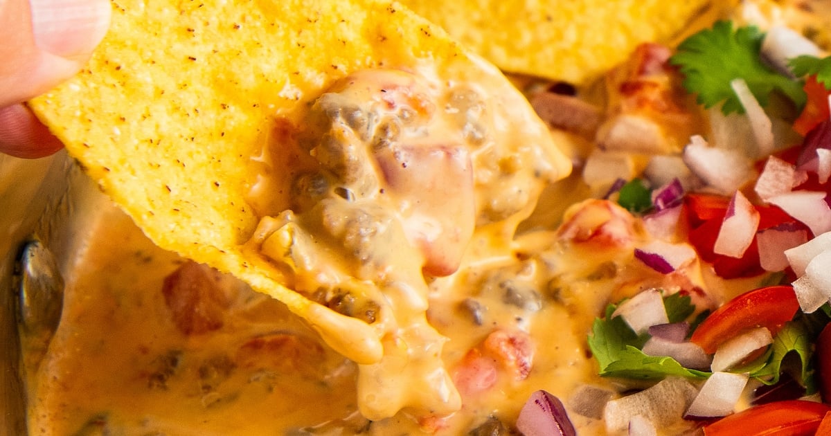 Someone scooping Rotel sausage dip onto a tortilla chip.