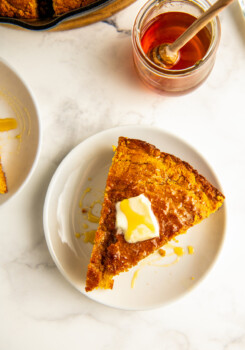 A slice of sweet potato cornbread with butter and honey on top.