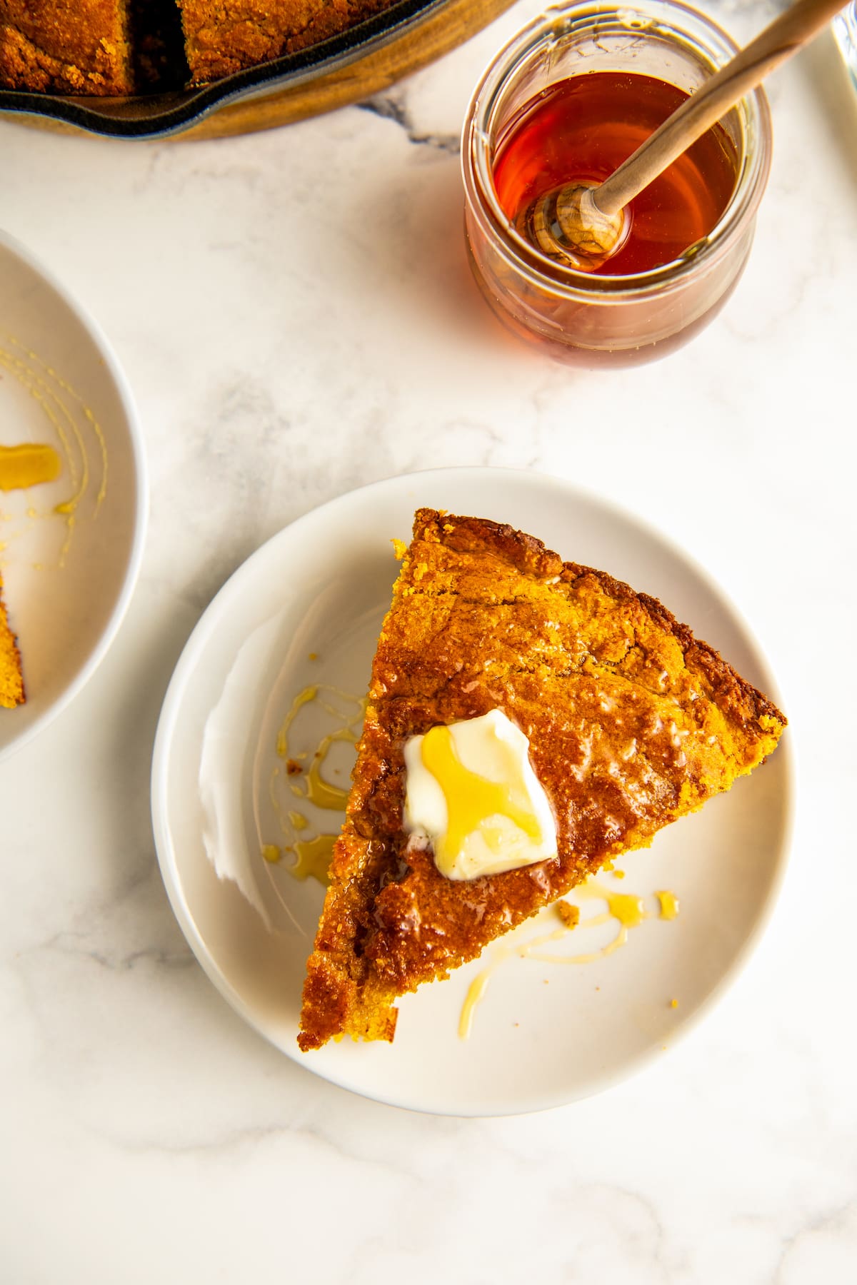 A slice of sweet potato cornbread with butter and honey on top.