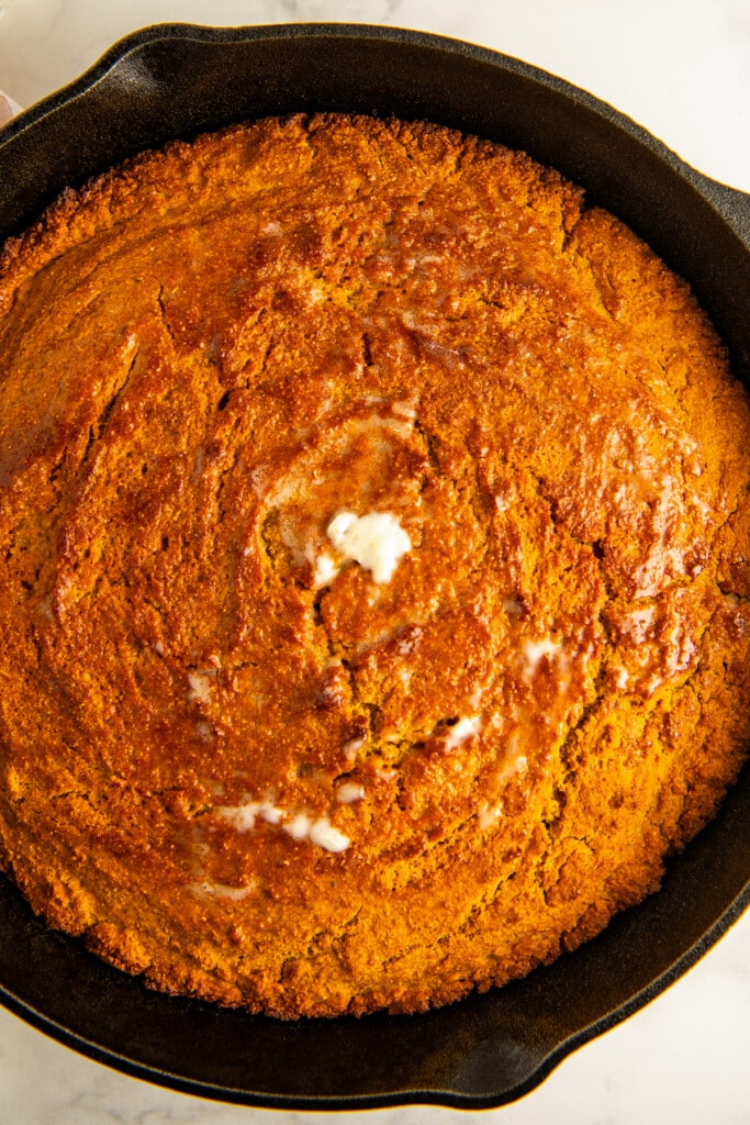 A cast iron skillet with sweet potato cornbread. Melted butter drizzled on top.
