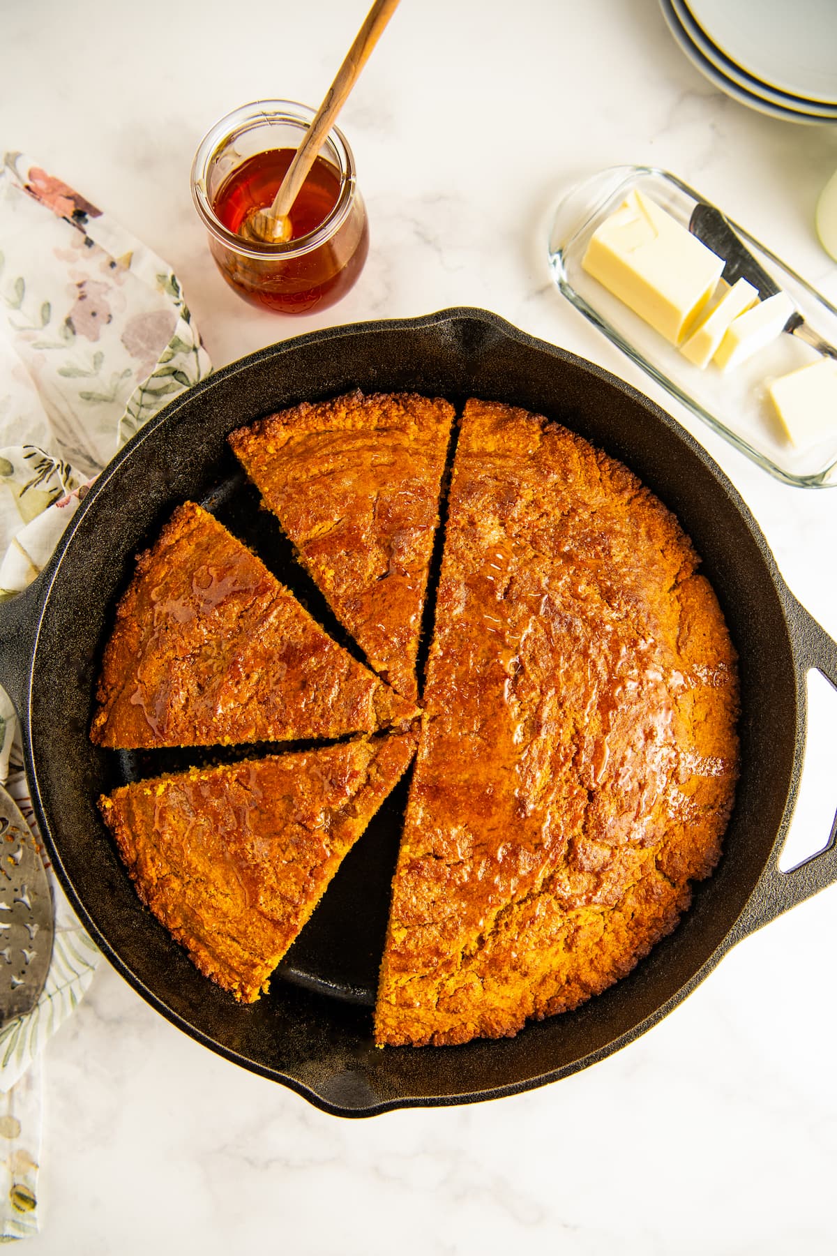 A skillet of sweet potato cornbread with a jar of honey and stick of butter in the background.