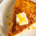 A slice of sweet potato cornbread on a plate with a pat of butter and honey.