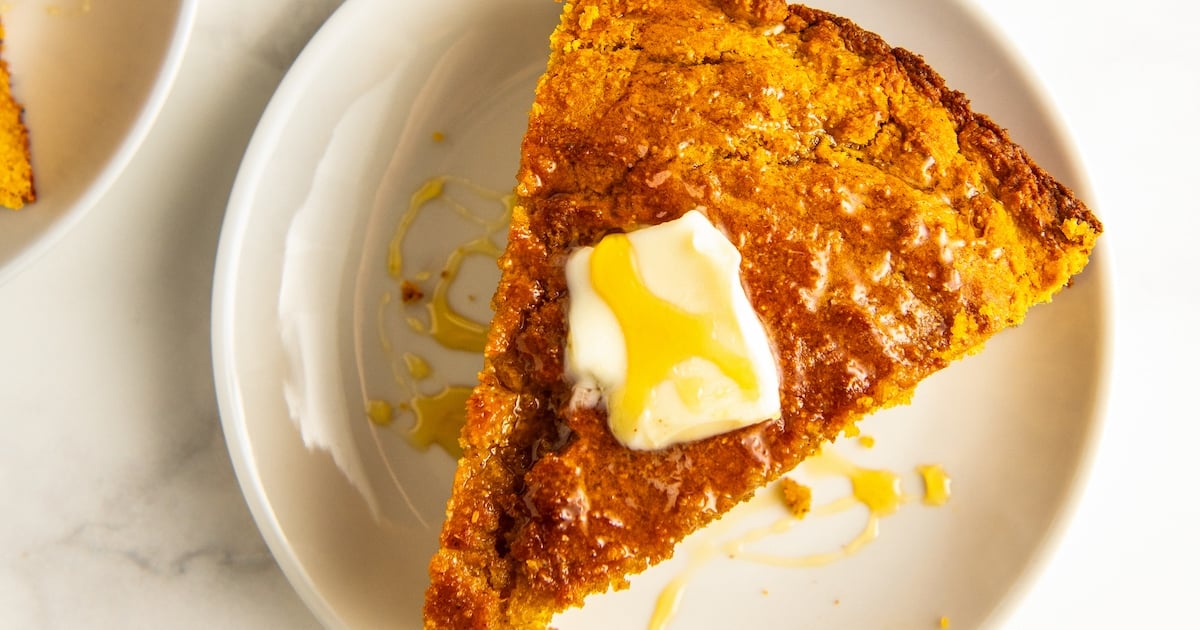 A slice of sweet potato cornbread on a plate with a pat of butter and honey.
