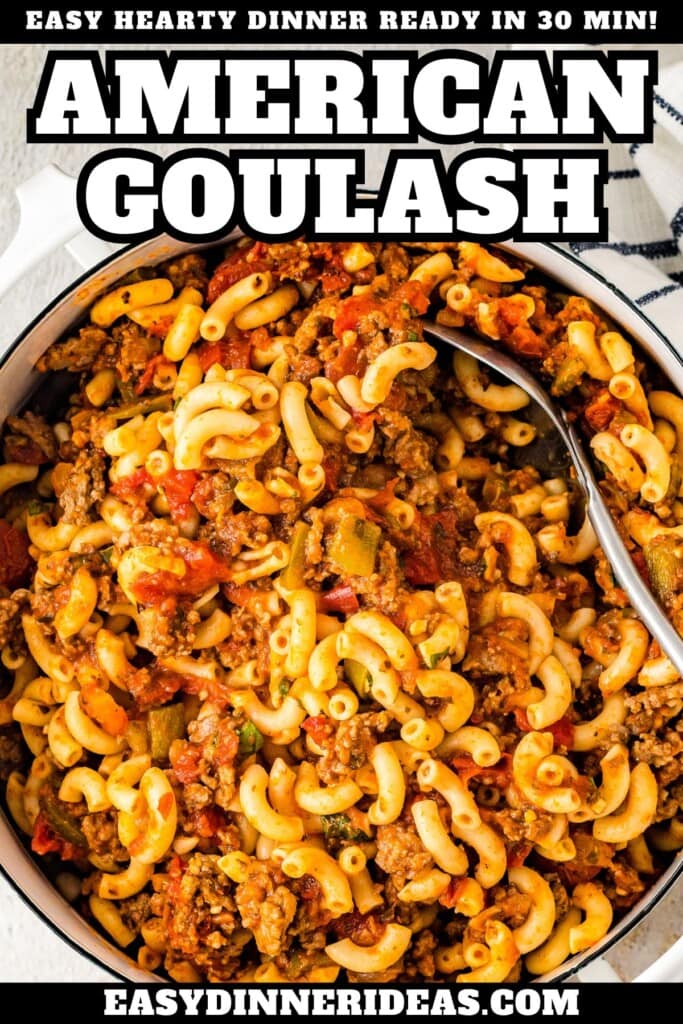An overhead view of a pot of american goulash with a spoon stuck into the pot for serving.