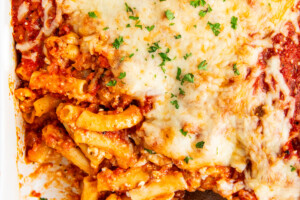 Cooked baked ziti being served with a wooden spoon.