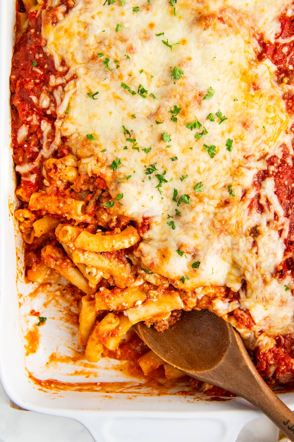 Cooked baked ziti being served with a wooden spoon.