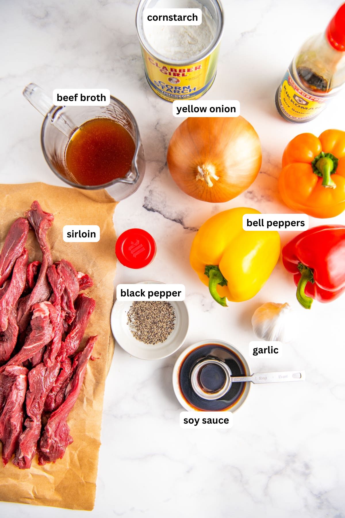 The ingredients for crockpot pepper steak recipe in order from top to bottom: cornstarch, beef broth, yellow onion, bell pepper, sirloin, black pepper, garlic and soy sauce.