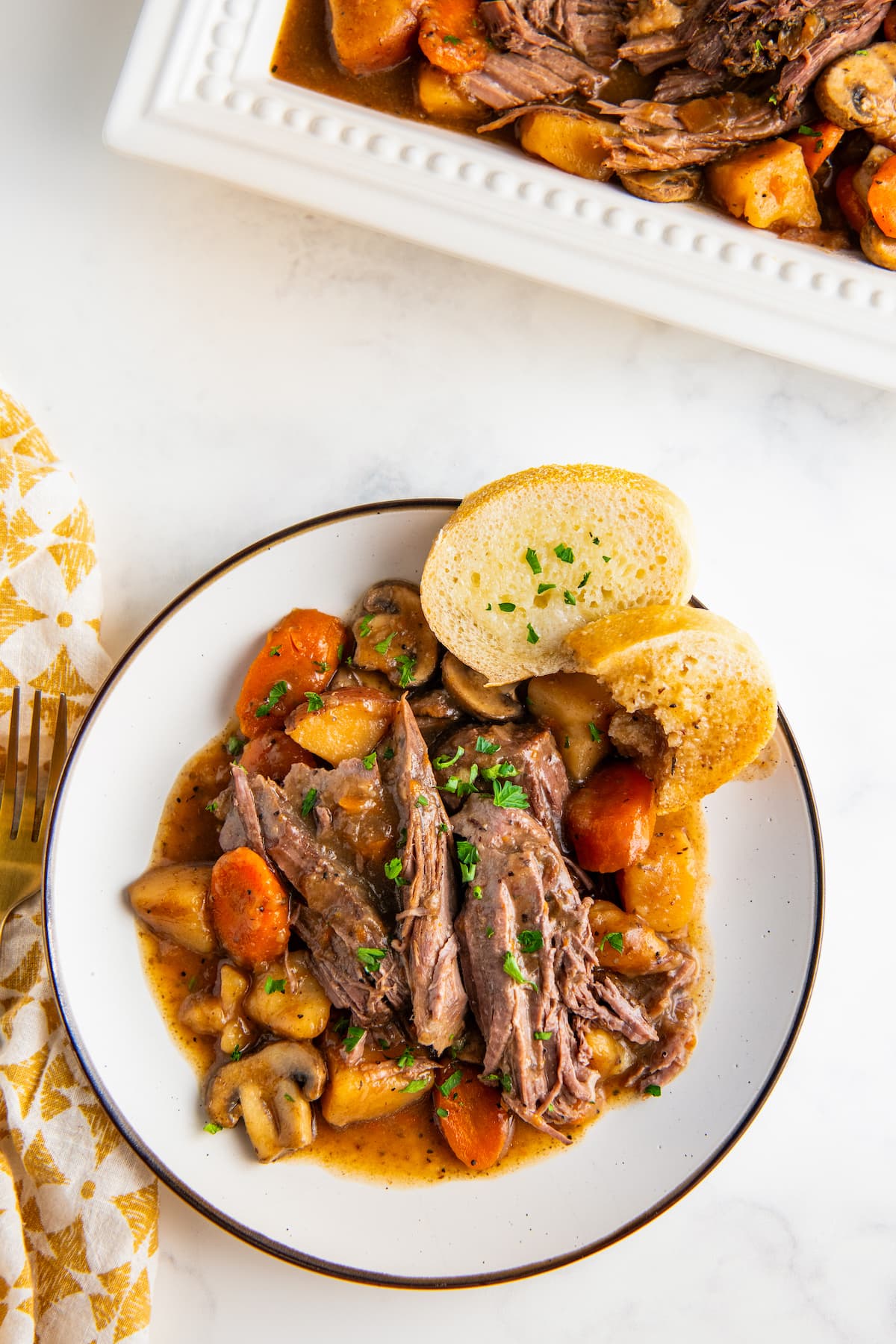A plate of shredded pot roast, veggies, and bread.