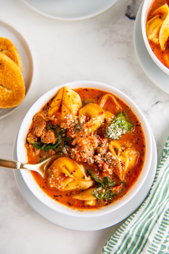 Close up of crockpot tortellini soup in a white bowl.