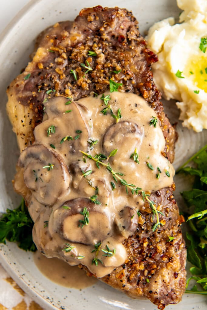Mushroom sauce on top of steak with a side of potatoes.