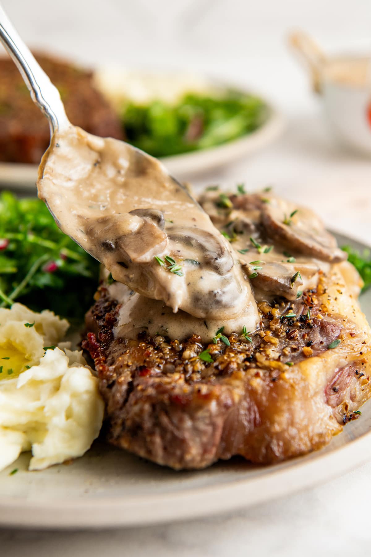 Spooning creamy mushroom sauce over a juicy steak with a side of potatoes and salad.