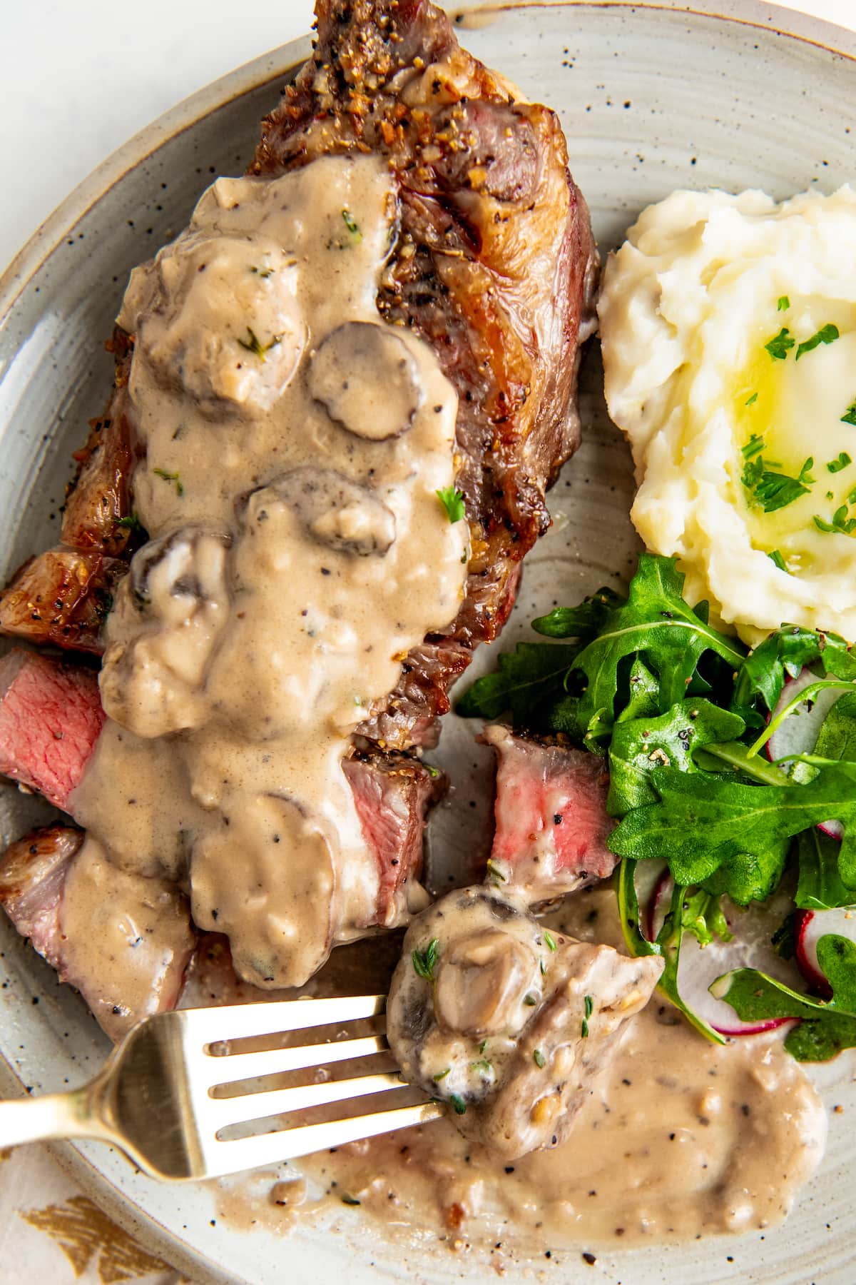 A bite of steak with mushroom cream sauce on a plate with a fork.
