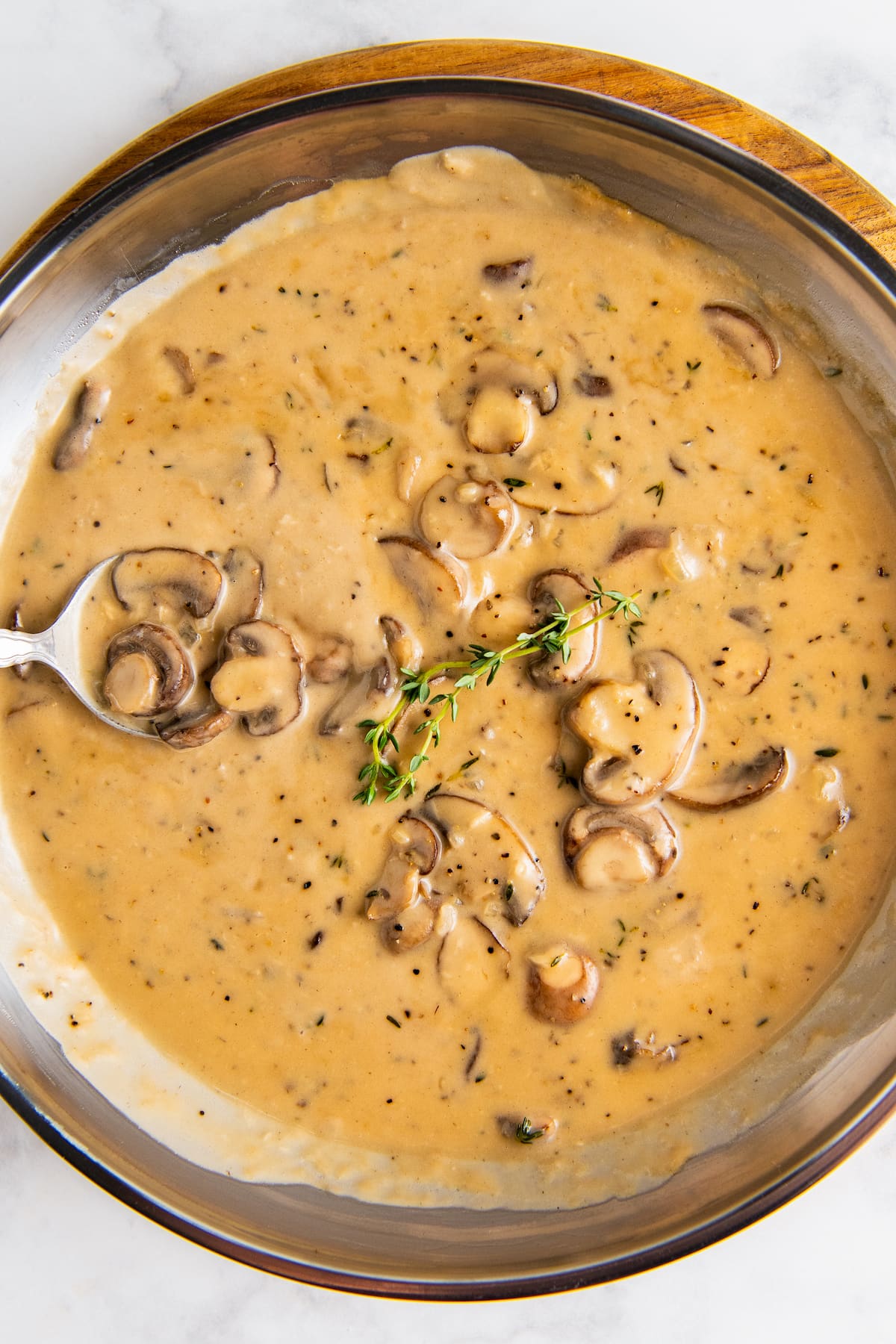 Finished mushroom sauce for steak in a skillet with a serving spoon and fresh herbs on top.