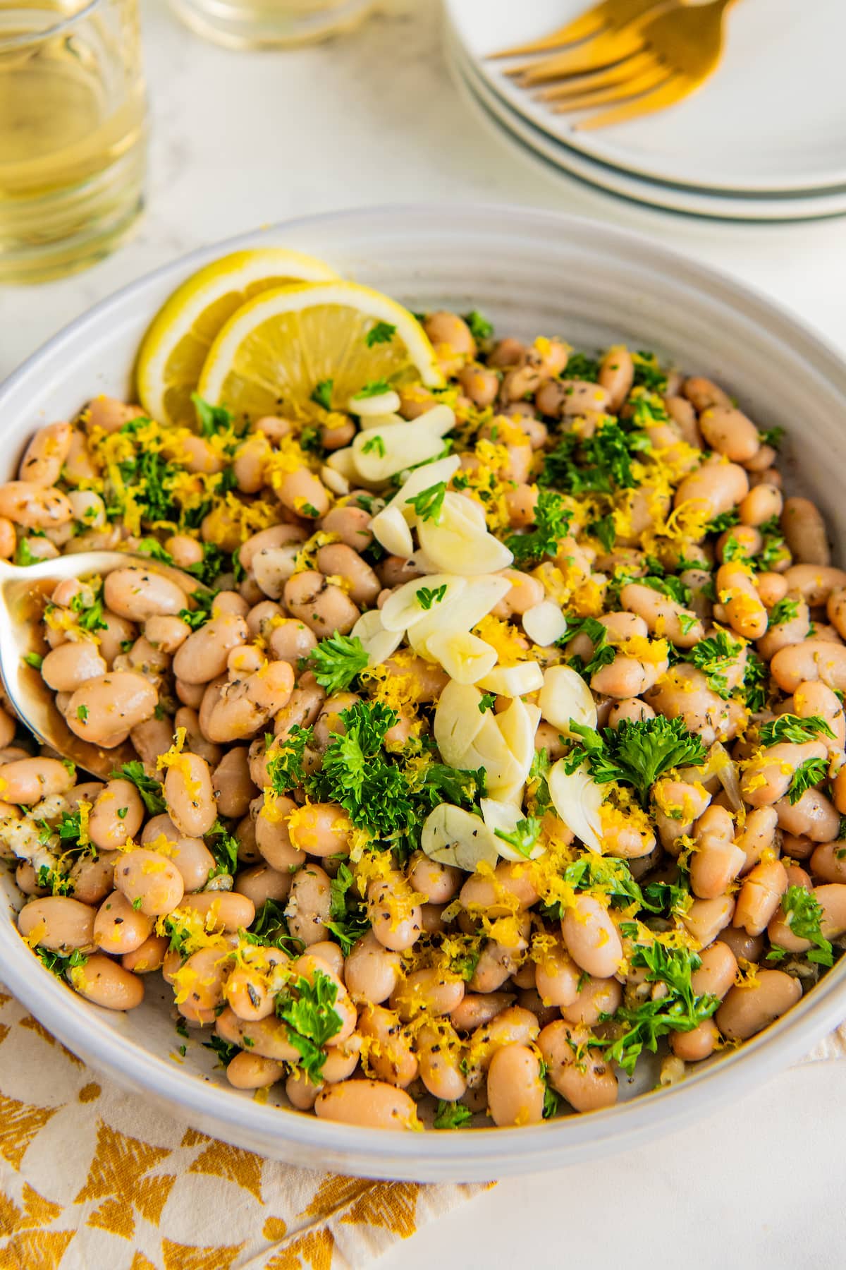 White bean salad in a white bowl garnished with fresh lemon zest and sliced garlic.