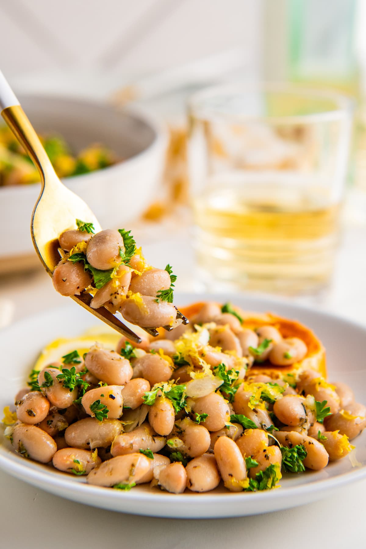 A fork lifting a bite of white bean salad off a plate. 