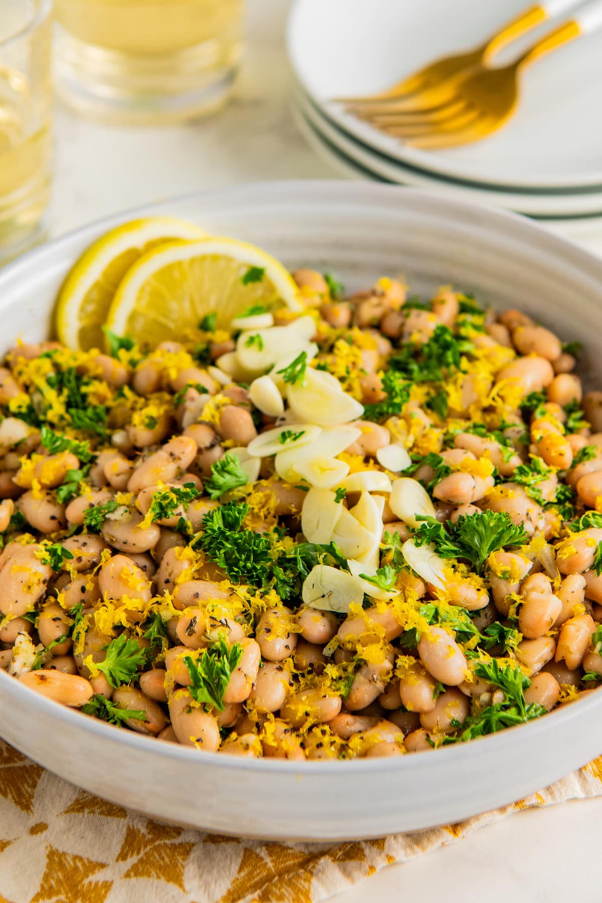A large white bowl full of easy white bean salad garnished with sliced garlic, lemon zest and freshly minced curly parsley.