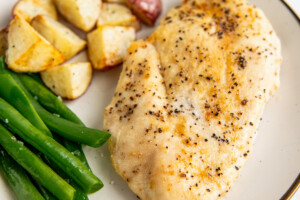 A plate with baked chicken breast, roasted potatoes, and green beans.