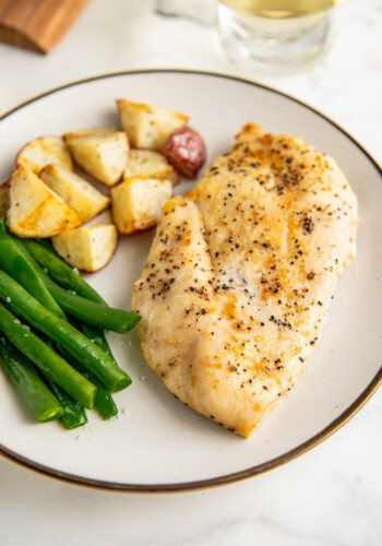 A plate with baked chicken breast, roasted potatoes, and green beans.