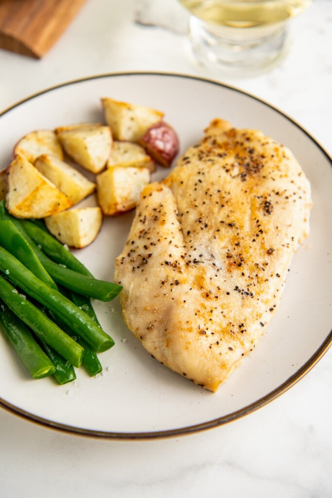 A plate with baked chicken breast, roasted potatoes, and green beans.