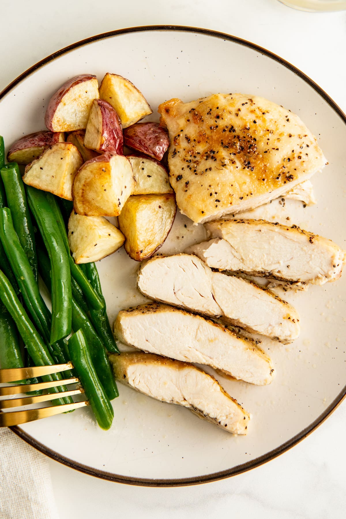 Sliced chicken breast on a plate with green beans and potatoes.