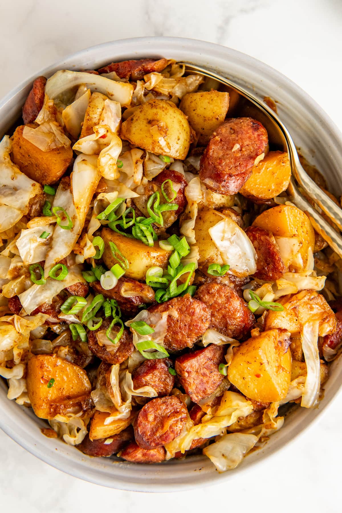 Serving a portion of cabbage, sausage, and potatoes with a large spoon.