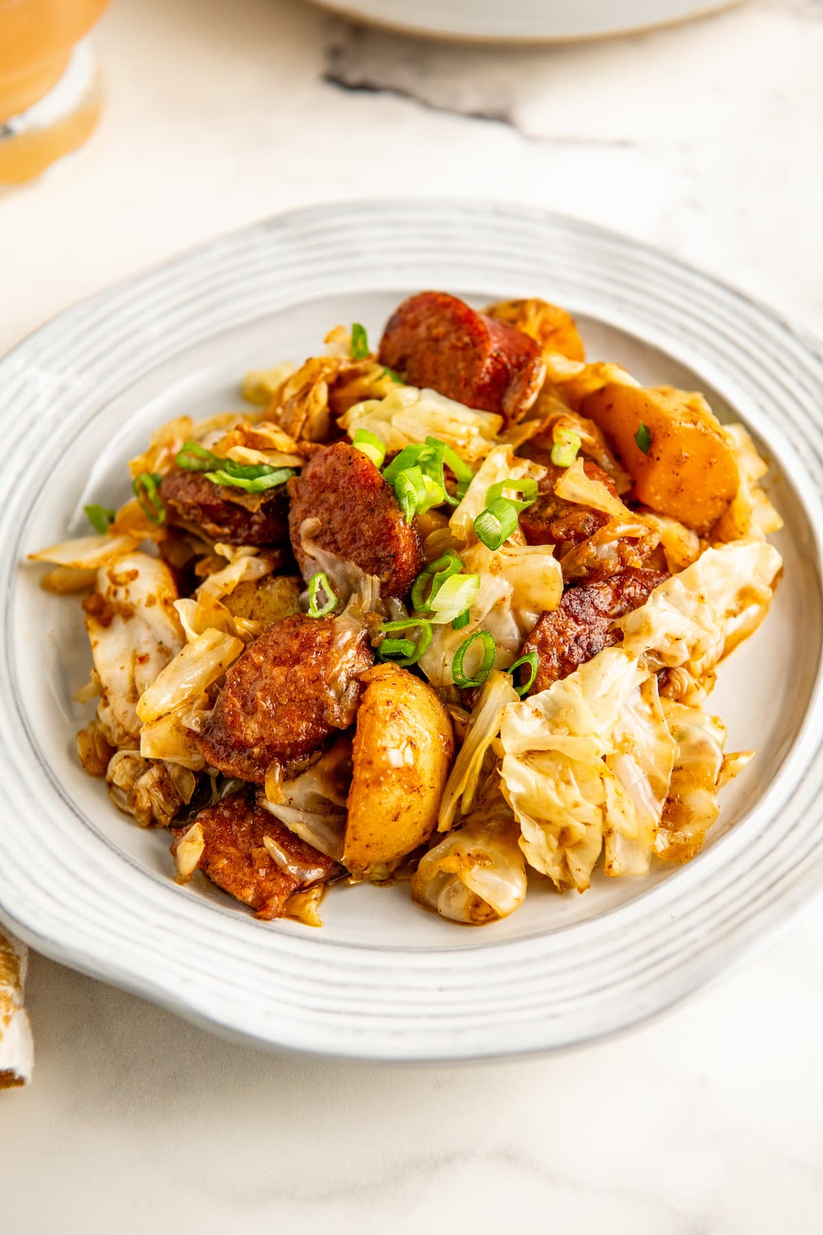 A white plate with cabbage, sausage, and potatoes.