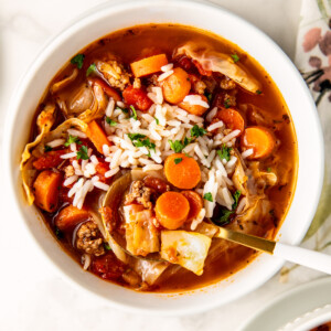 A white bowl with cabbage roll soup and a spoon.