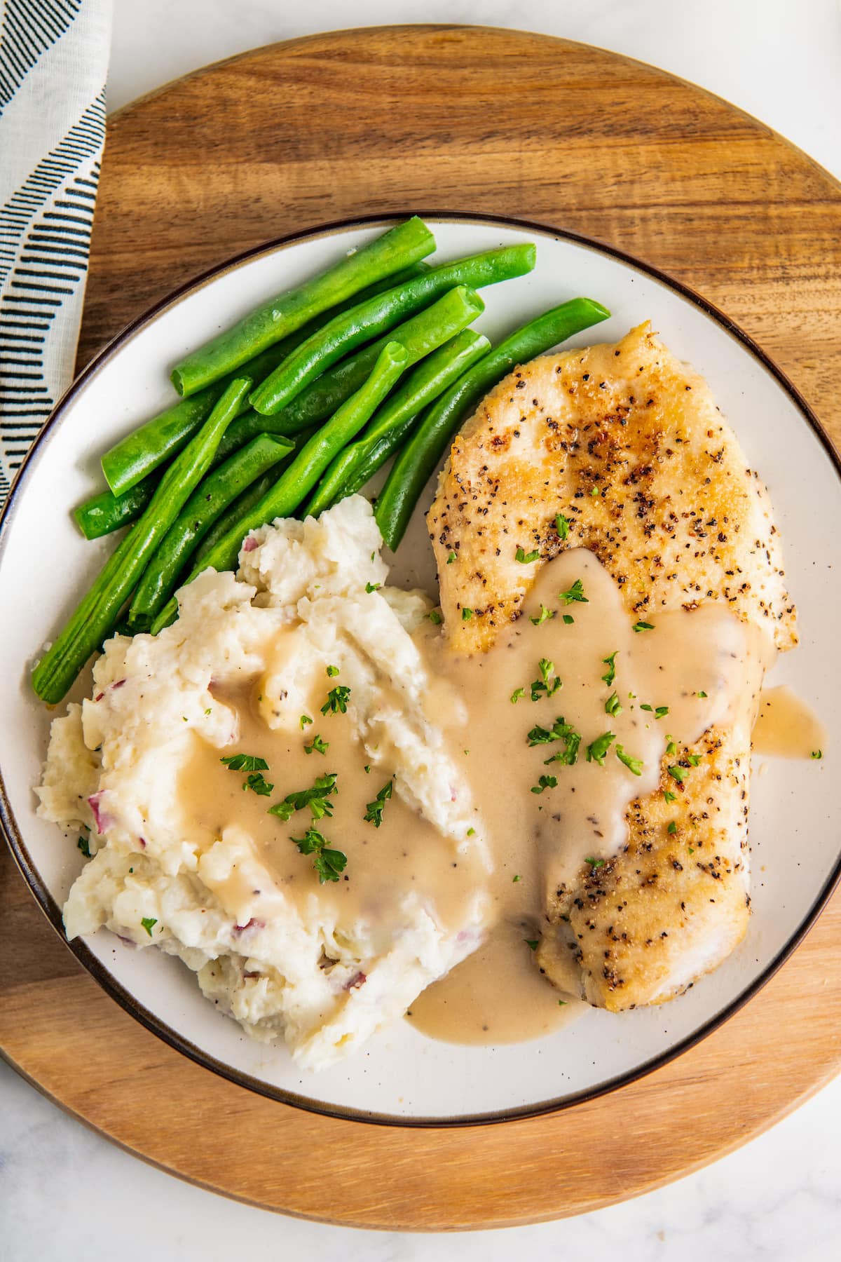 A plate with chicken and mashed potatoes smothered in gravy and green beans on the side.