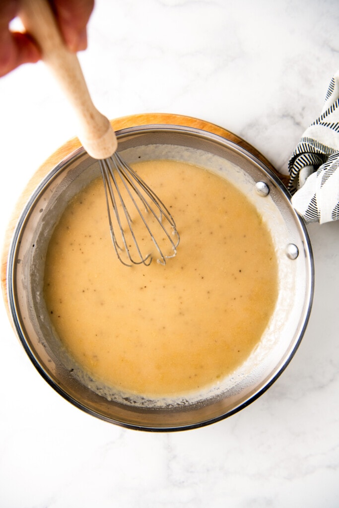 Whisking the gravy as it cooks in a skillet.
