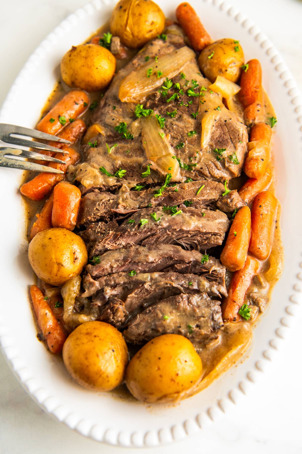 A white serving plate with sliced London broil, potatoes, and carrots.