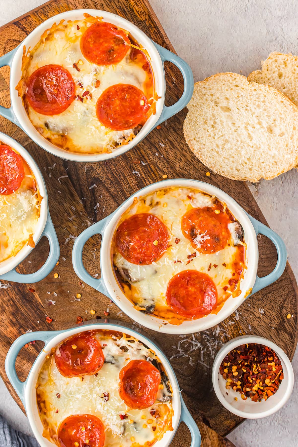 Pizza bowls on a serving board with small bowls of parmesan and red pepper flakes.